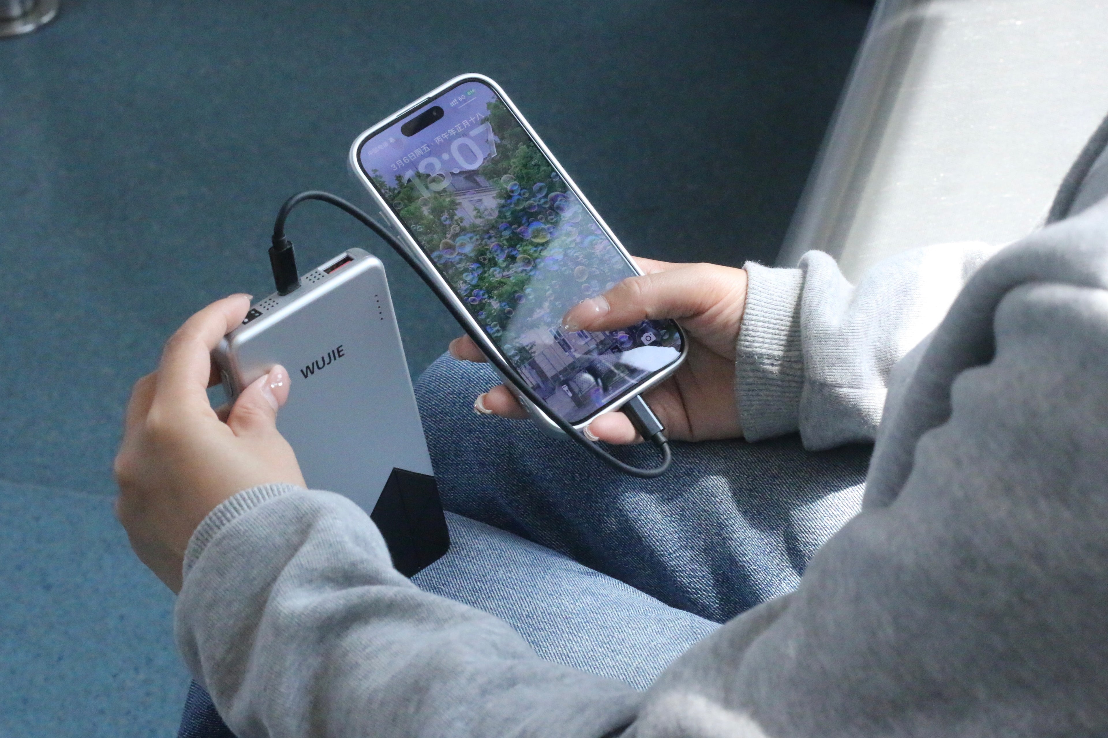 Hands using a WUJIE power bank to charge a smartphone, ensuring the device remains powered in the evening, symbolizing how technology offers convenient connectivity and ongoing support in daily life.