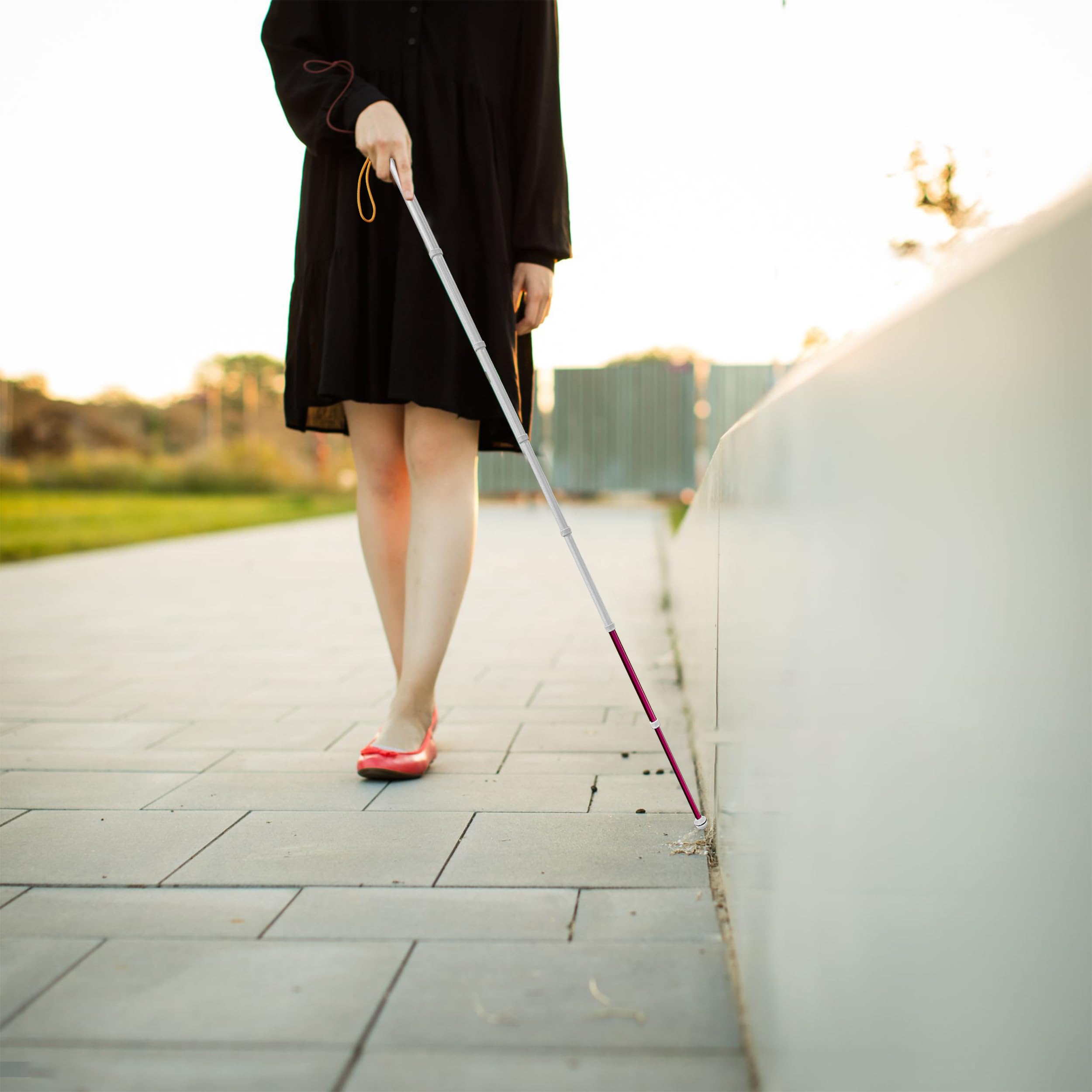 Visually impaired woman walking outdoors using extended telescopic blind cane along sidewalk curb
