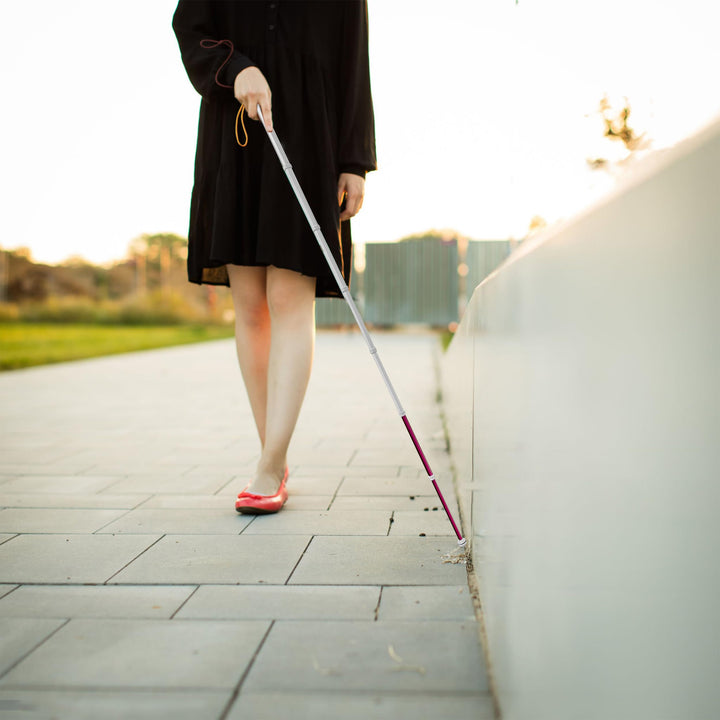 Visually impaired woman walking outdoors using extended telescopic blind cane along sidewalk curb