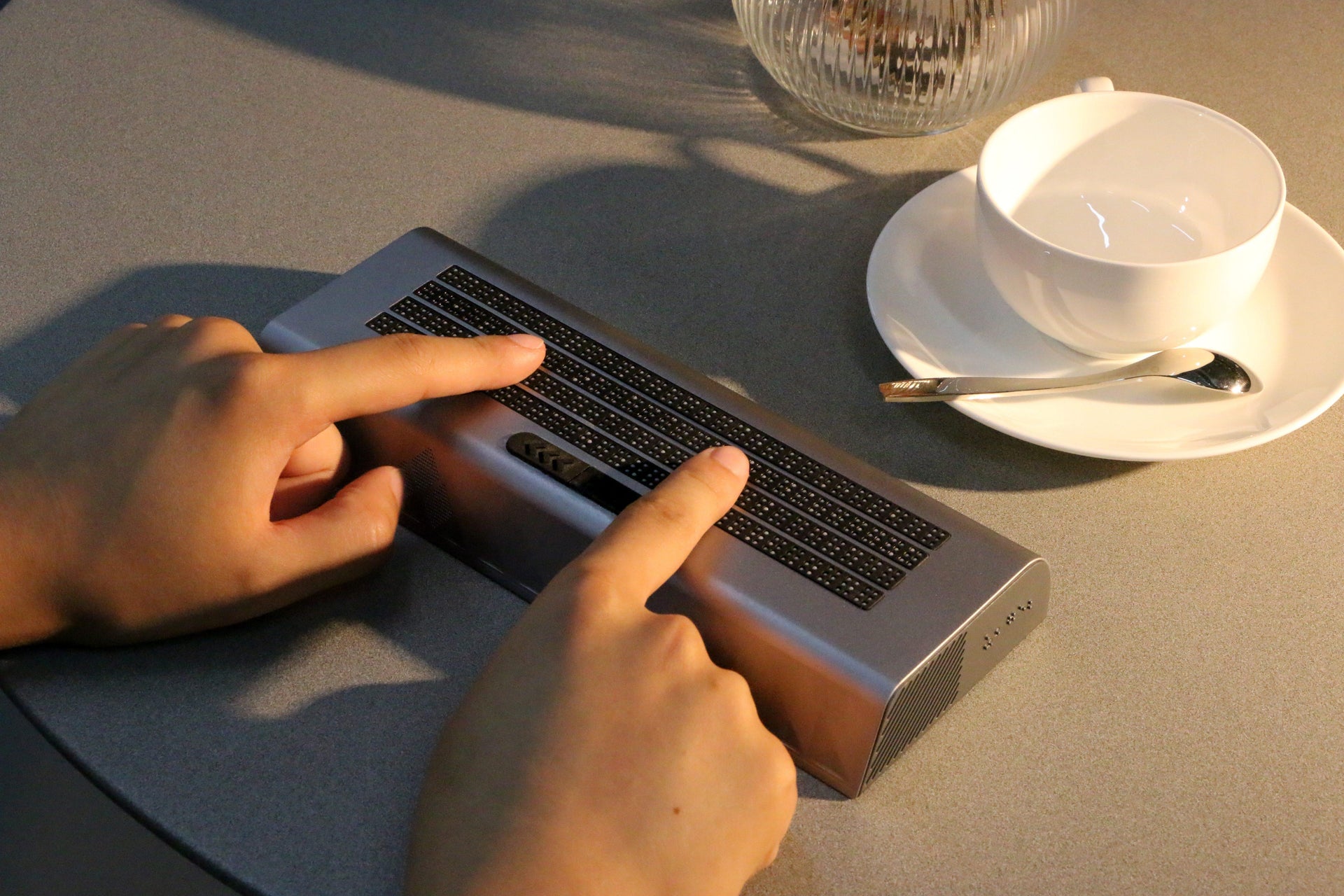 User reads braille by touching Zeta‑120 multi‑line braille display with both hands on table, real‑world daily‑use scene for blind users